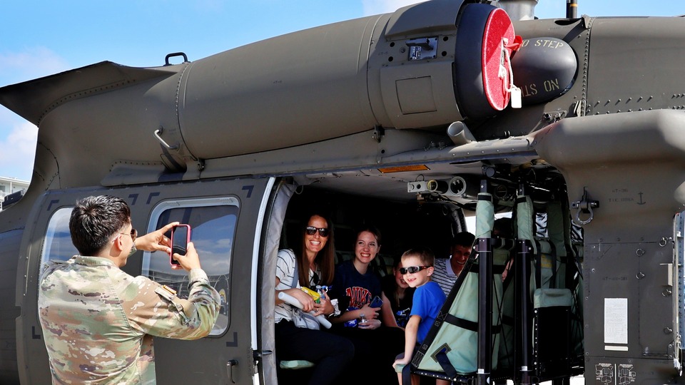 A man in the military takes a photo of a family at the Fan Midway during the PPG Presents Armed Forces Qualifying